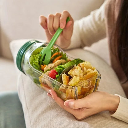 Person holding a glass container with a salad and a green fork.